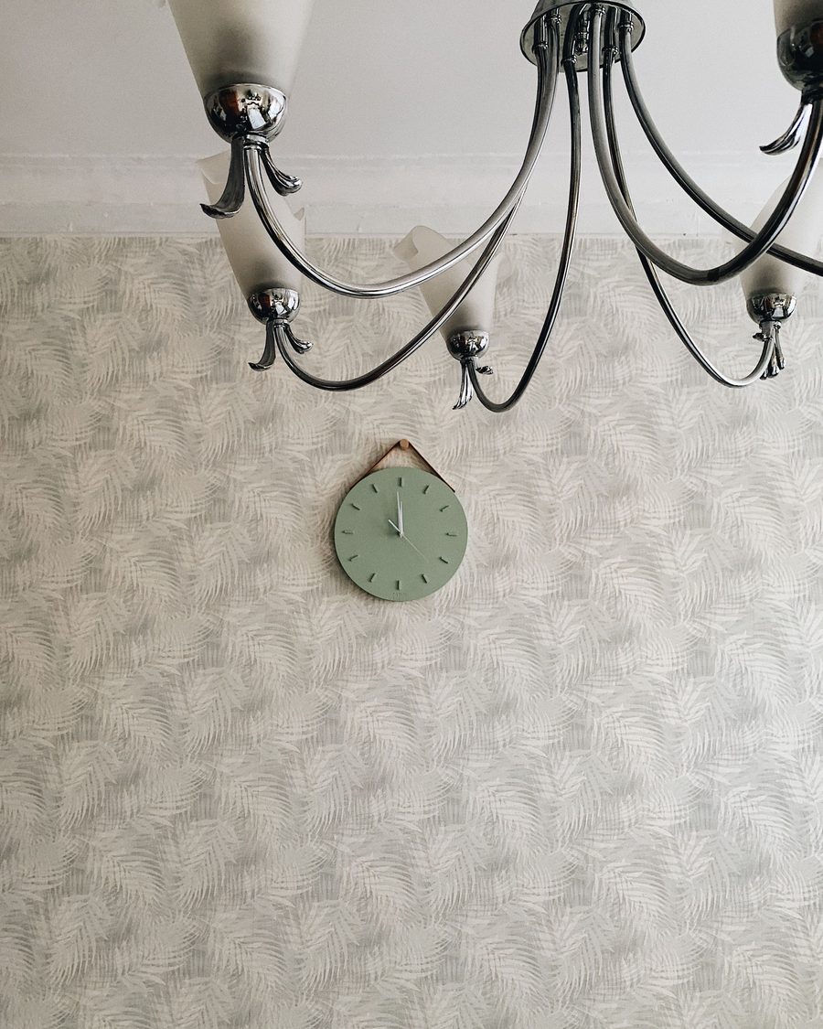 Small sage-green wall clock on a subtle cream palm-leaf textured wallpaper