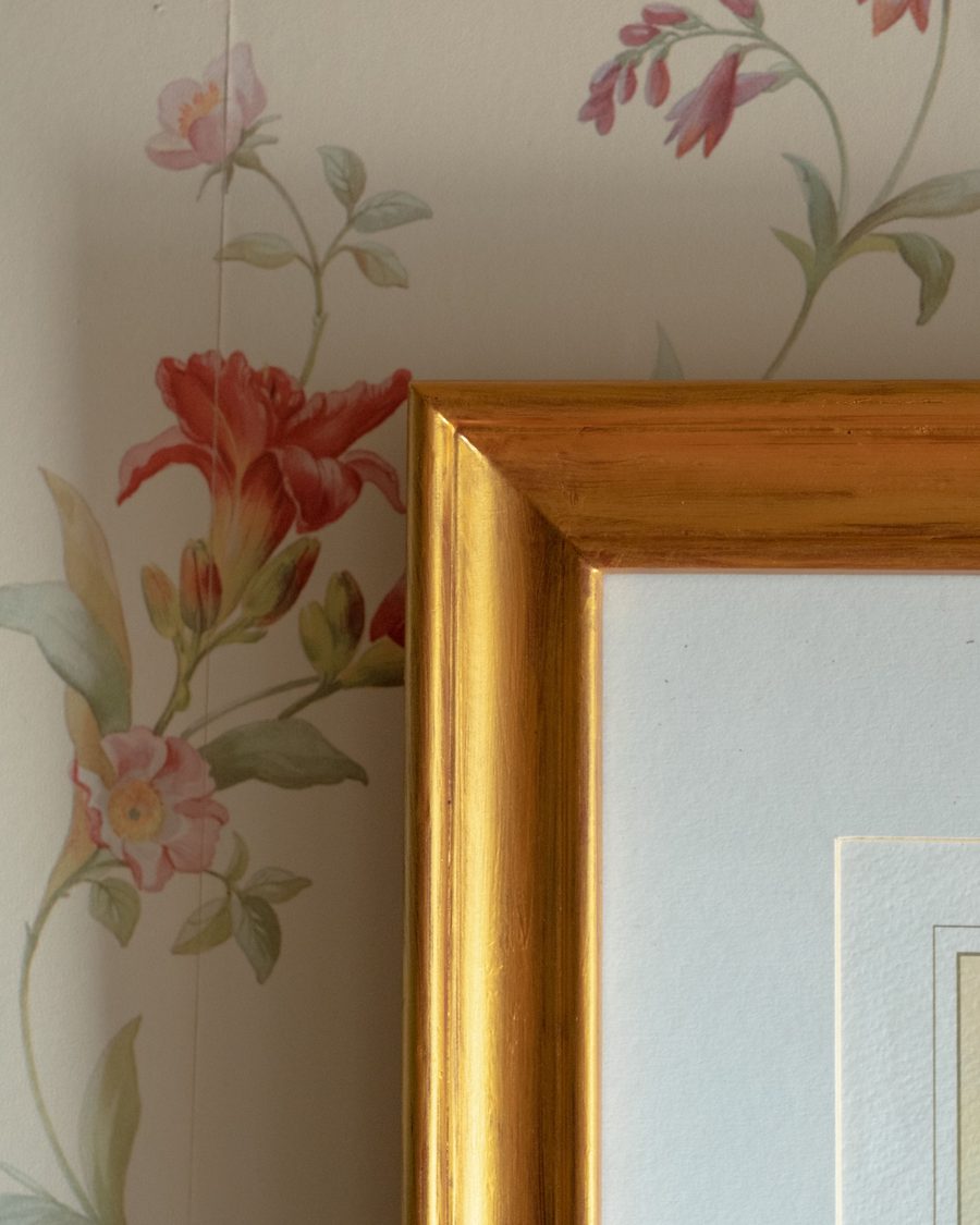 Corner of a gilded picture frame against pale pink lily wallpaper
