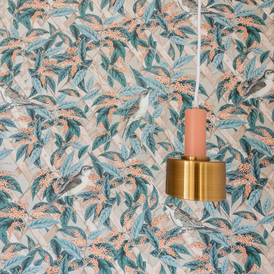 Close view of a teal and peach botanical wallpaper with leaves and small birds, a brass pendant lamp hanging in front of it
