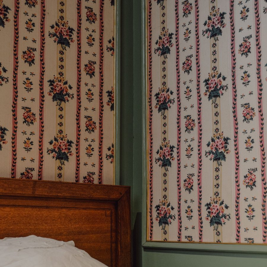 Striped floral wallpaper meeting sage-green painted trim above a wooden bed headboard