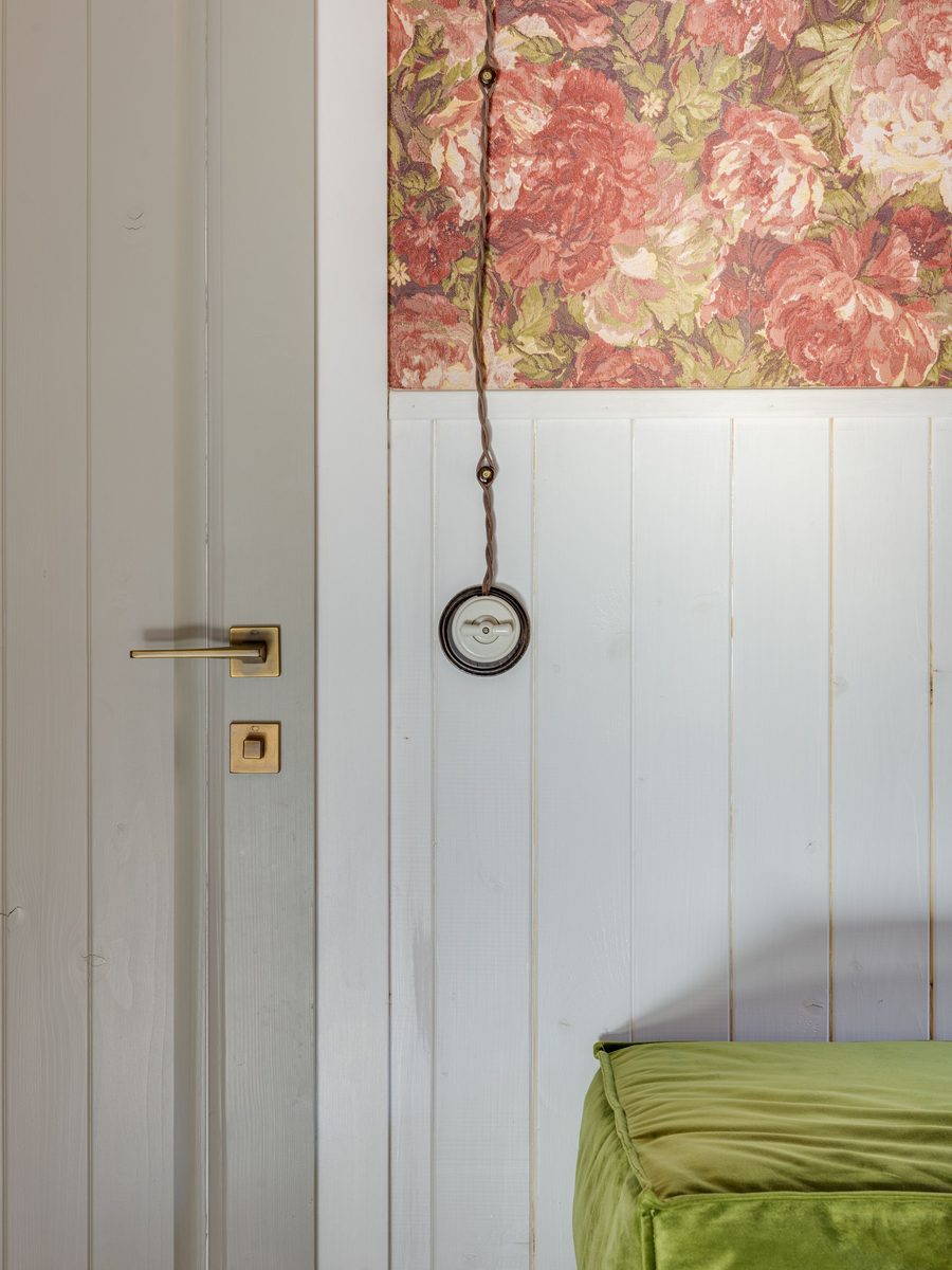 Red peony wallpaper meeting white tongue-and-groove wainscot panelling beside a white door with a brass handle