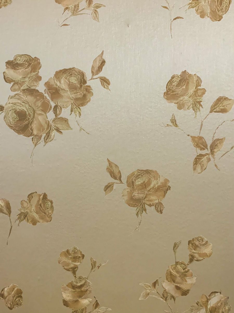 Close-up of cream wallpaper with a tonal gold rose print in soft natural light